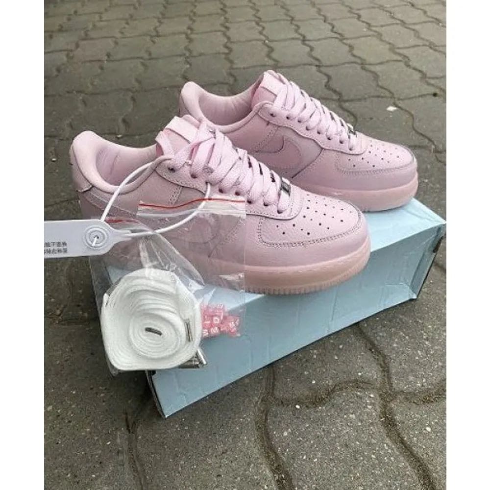 nike-nocta-air-force-1-low-pink-girls-for-women-bsf372 | UAE SPORT STORE Pink Nike-style sneakers with white laces on a light blue shoebox; spare laces in clear bag visible outdoors.