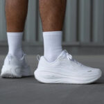 Close-up of white running shoes with curved midsoles, worn with white socks.