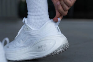nike-vomero-plus-heel-tab-23479845-1080 | UAE SPORT STORE Person slides on a white Nike running shoe, pulling the heel loop to adjust the fit.