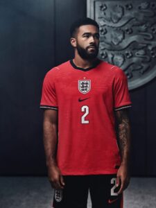 nss-maglie-mondiale-2026-inghilterra-2 | UAE SPORT STORE Male footballer in a red England jersey with number 2, standing against a dark backdrop.