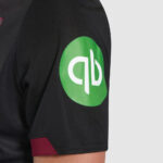 Close-up of a black short-sleeve shirt sleeve with a bright green circular logo containing white 'qb' letters.