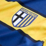 Parma Calcio crest on a bright yellow jersey with blue trim and striped motif in the background.