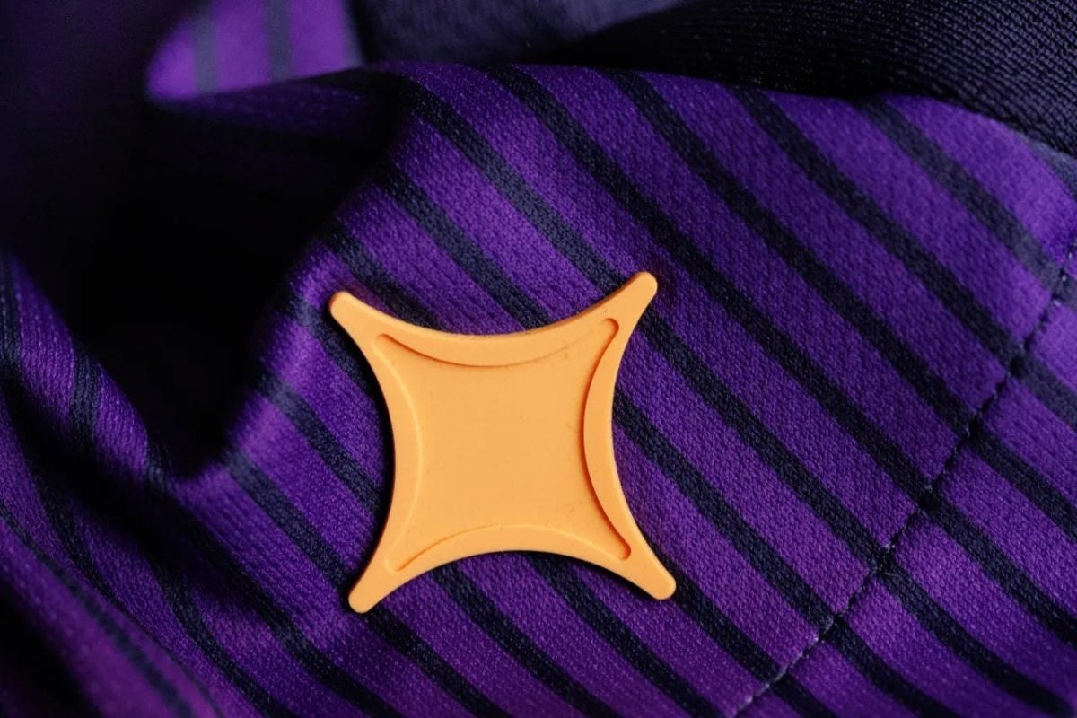 Orange curved-square pin on purple striped fabric (likely a jacket lapel).
