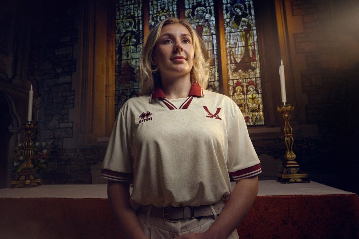 Young woman in a cream polo with burgundy trim stands at an altar in a church with stained glass behind her.