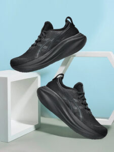 Pair of black athletic running shoes suspended against a light blue backdrop with white geometric props behind them