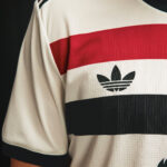 Close-up of a cream jersey with red, white, and black horizontal stripes and the Adidas trefoil logo.