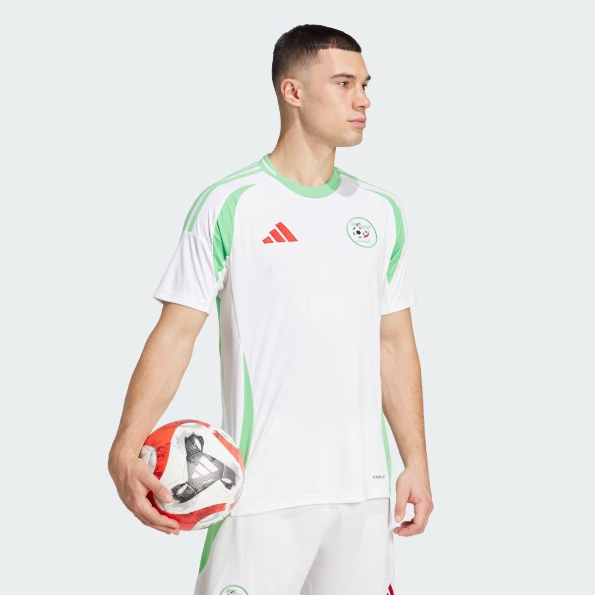 Soccer player in a white and green kit holding a red-and-white ball, facing right against a light gray background.