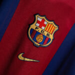 Close-up of the FC Barcelona crest on a red-and-blue striped soccer jersey with a yellow Nike swoosh visible beyond the badge.