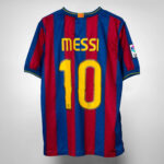 Back view of FC Barcelona jersey with blue and maroon vertical stripes, displaying the yellow 'MESSI' name and the number '10'. On the sleeve patch visible.