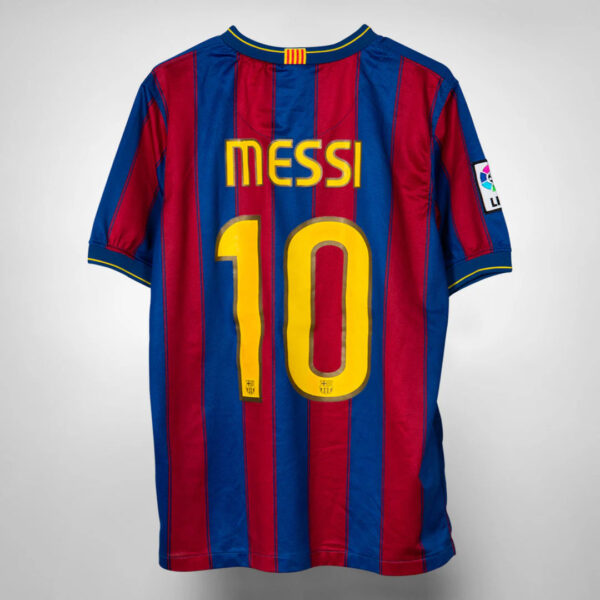 Back view of FC Barcelona jersey with blue and maroon vertical stripes, displaying the yellow 'MESSI' name and the number '10'. On the sleeve patch visible.