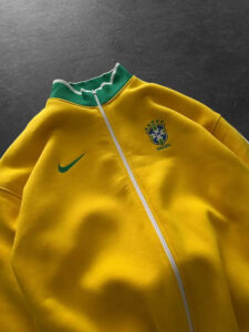 Yellow Brazil track jacket with a green collar, white zipper, and the Brazil crest on the chest along with a green Nike swoosh on the left sleeve area (informative sports apparel image).