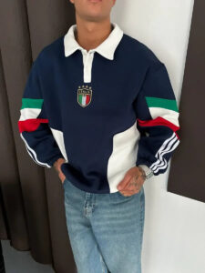 Person wearing a navy rugby shirt with a white collar, Italian crest, and green/white/red striped sleeves, paired with jeans.