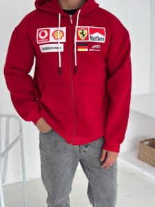 Person wearing a red zip-up hoodie with sponsor logos on the chest and drawstrings hanging down, hands in pockets.