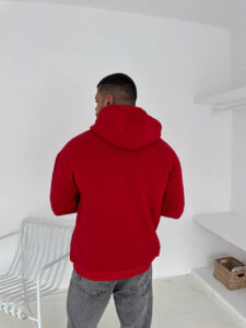 Man wearing a red hoodie seen from the back in a bright white room, gray jeans, and short haircut.