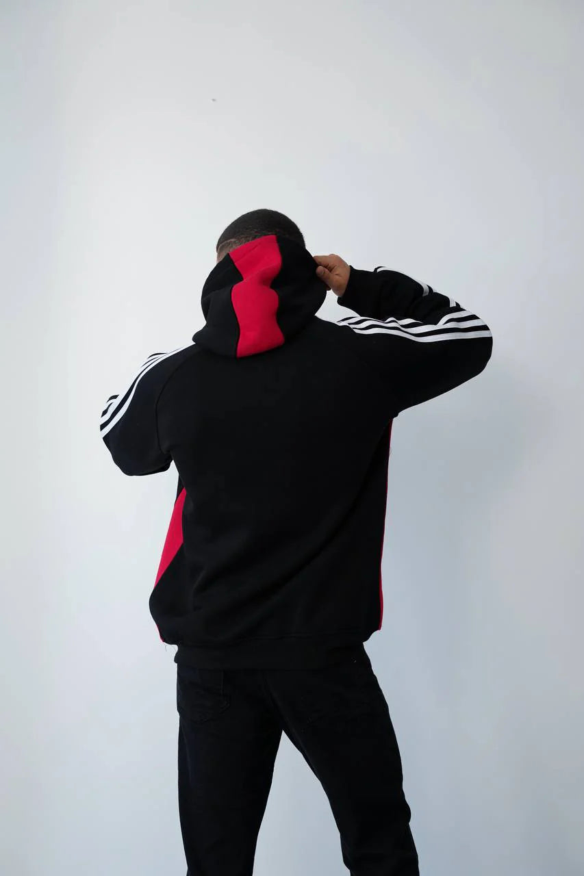 photo_2025-11-09_15-10-56 | UAE SPORT STORE Person seen from behind wearing a black hoodie with red panels, adjusting the hood against a plain white wall.