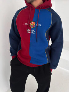 Man wearing a color-block red and blue FC Barcelona hoodie with crest and white text on the chest