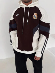 Person wearing a Real Madrid hoodie with maroon front, white sleeves, and striped arms, standing in a neutral space.