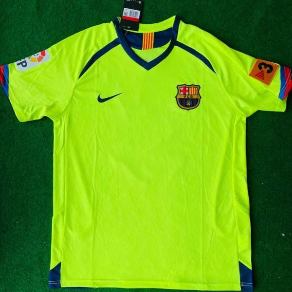 Neon yellow FC Barcelona goalkeeper jersey laid on green turf with club crest, Nike logo, and league patches on sleeves.