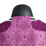 Back view of a pink patterned jacket on a dark mannequin, showing purple sleeves and a striped collar.