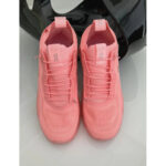 Pair of pink athletic sneakers with laces, placed side by side on a light surface, a dark helmet in the background