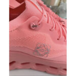 Close-up of pink athletic sneaker showing laces, eyelets, and knit fabric with a light gray logo on the midsole.