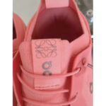 Close-up of a pink sneaker tongue with a gray embroidered logo and pink laces, showing the fabric and side tag.