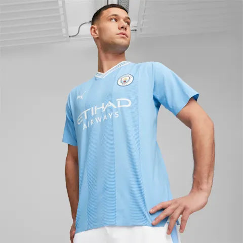 Male model wearing a light blue Manchester City away jersey, standing with hands on hips, sponsor 'Etihad Airways' visible on the chest.