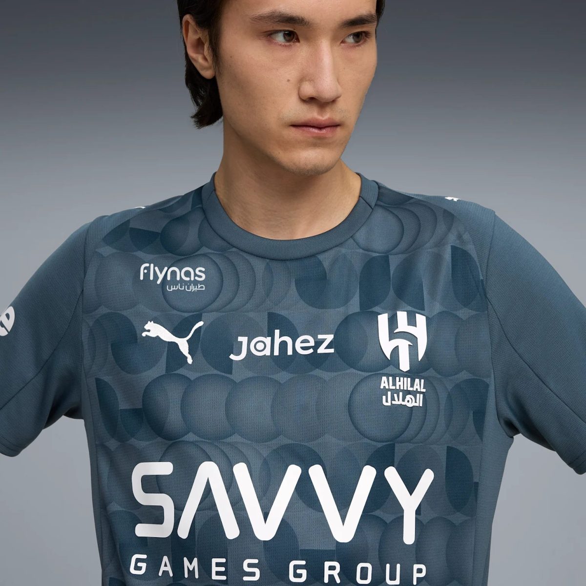 Close-up of a man wearing a dark blue geometric-pattern esports jersey, looking to the right, with sponsor logos on the chest area.