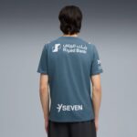 Back view of a person wearing a blue T-shirt with Riyad Bank logo and 'SEVEN' text on the lower back area.
