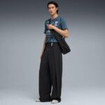 Male model wearing a teal patterned T-shirt, oversized black wide-leg pants, white sneakers, and a black shoulder bag with keys hanging from the strap.