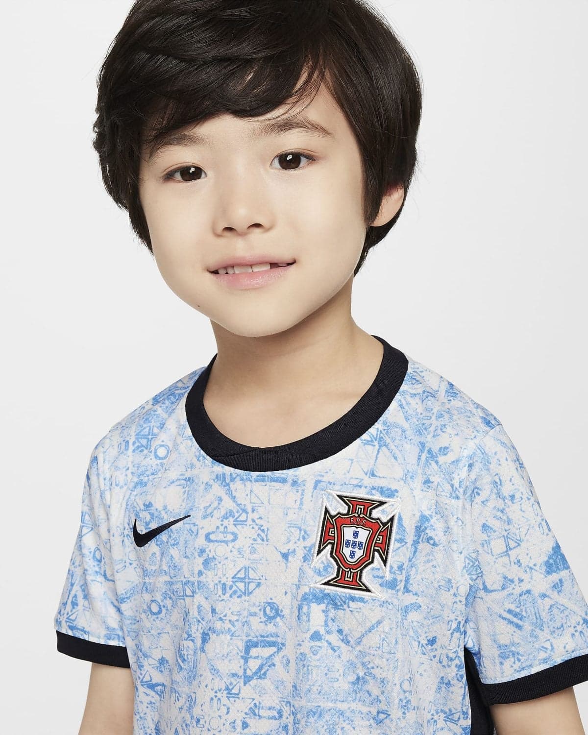 Close-up portrait of a smiling young person with short dark hair, wearing a light blue Portugal football jersey with a black collar and crest visible on the chest.