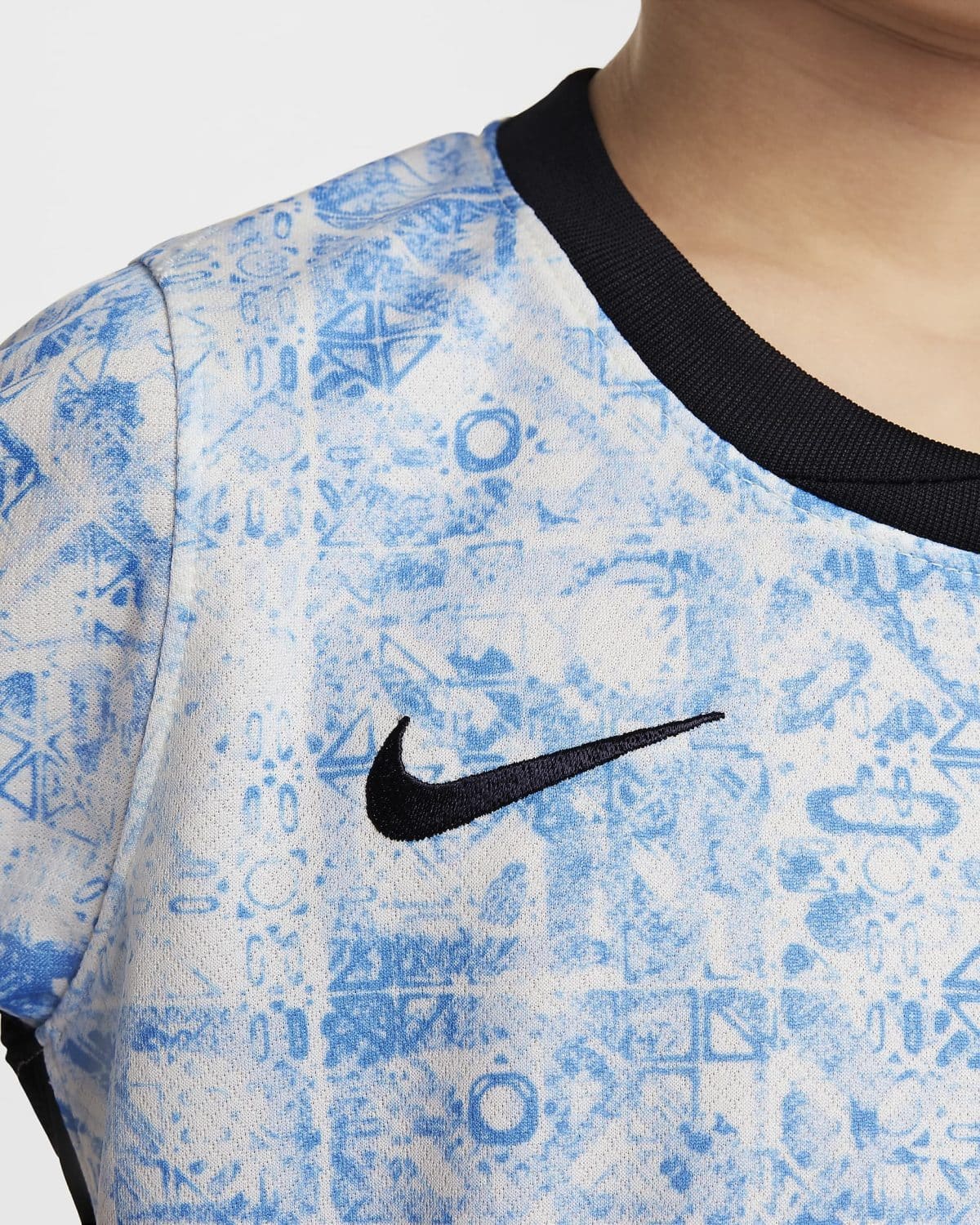 Close-up of a blue and white patterned shirt showing a black ribbed collar and a black Nike swoosh logo near the chest area.