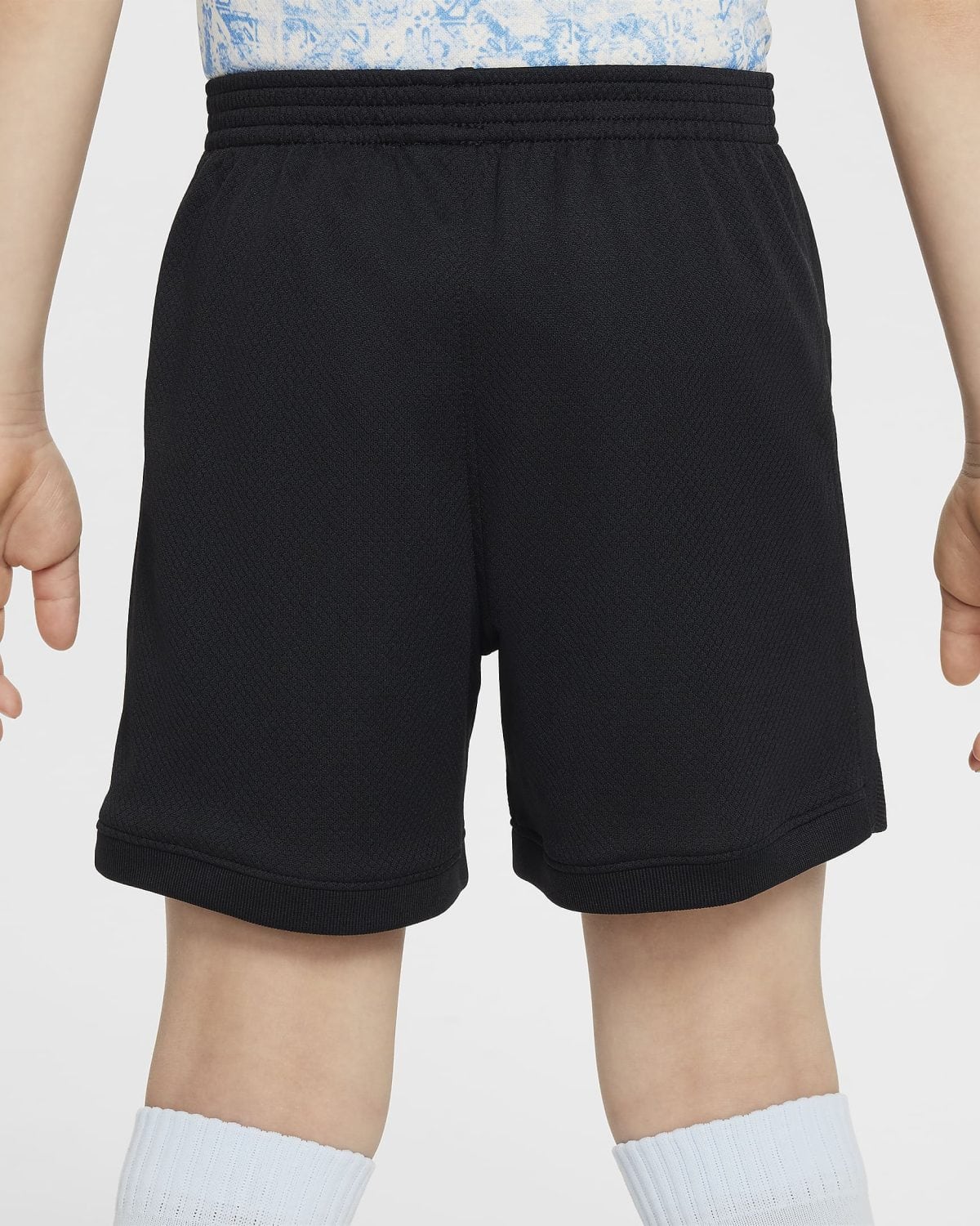 Back view of a person wearing black athletic shorts with a thick elastic waistband, blue patterned shirt, and light blue ribbed socks.