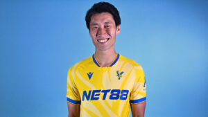 Smiling man in a yellow soccer jersey against a blue background, posing for a portrait.