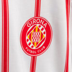 Circular Girona Futbol Club crest on a white jersey with red stripes.