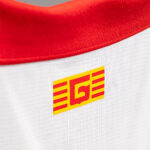 Close-up of a white fabric jersey with a red collar and a yellow-red brand logo on the chest area.