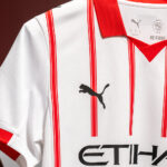 Close-up of a white football jersey with red vertical stripes, red collar, and a black Puma logo on the chest.