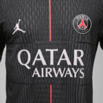 Close-up of a dark gray Paris Saint-Germain jersey with a pink center stripe, featuring the Jumpman logo and PSG crest, plus QATAR AIRWAYS sponsor text.