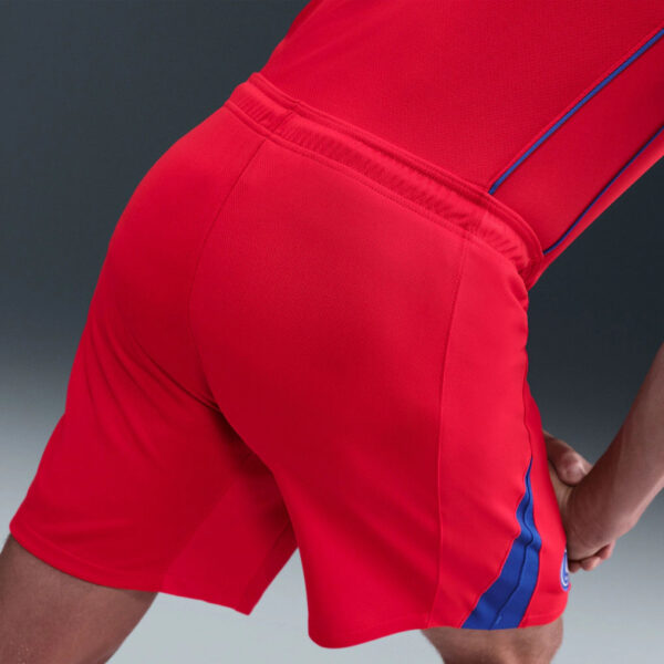 Close-up of red athletic shorts with a blue side stripe and elastic waistband detail.