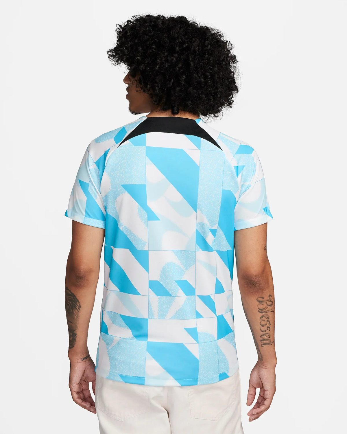 Back view of a person wearing a blue and white geometric shirt, with curly black hair visible from behind, against a light background.