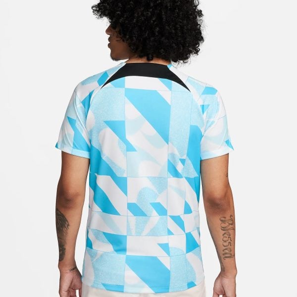Back view of a person wearing a blue and white geometric shirt, with curly black hair visible from behind, against a light background.