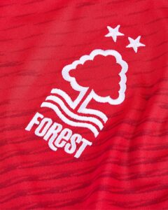 Close-up of red fabric showing the Nottingham Forest FC crest in white, with wavy lines, a tree-like emblem, and two stars in the corner.