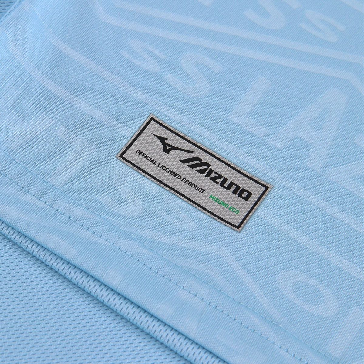 Close-up of light blue fabric with a rectangular Mizuno label that reads 'Official Licensed Product' and 'Mizuno Eco' in green.