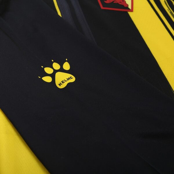 Yellow Kelme paw logo on black fabric, likely a sports garment