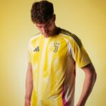 Young man wearing a yellow Juventus soccer jersey, looking down, against a pale yellow background.