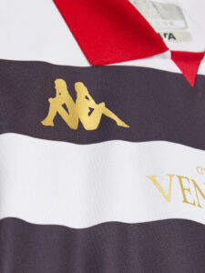 Close-up of a white jersey with a black horizontal stripe, gold Kappa logo, and red collar details.
