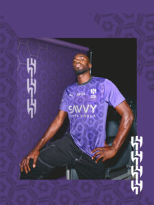 Athlete in a purple team jersey poses confidently against a purple patterned backdrop.