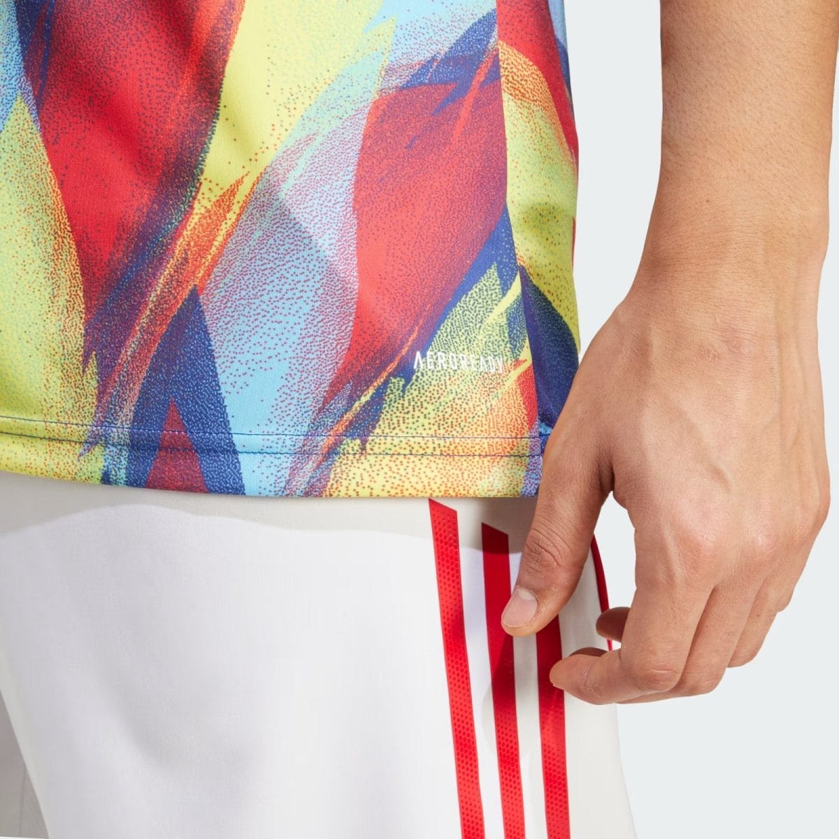 Close-up of a colorful abstract sports fabric with a hand resting nearby and a small 'AEROREADY' logo visible on the material.