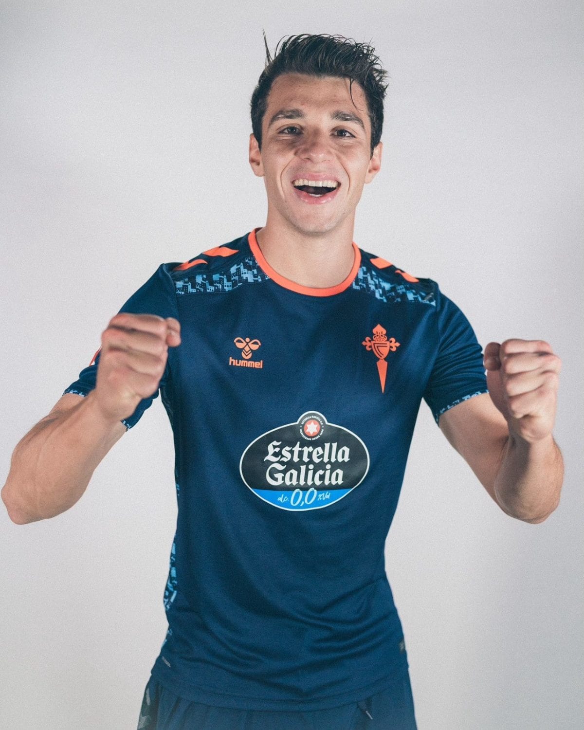 Young man in a blue sports jersey raises his fists in celebration, smiling at the camera.