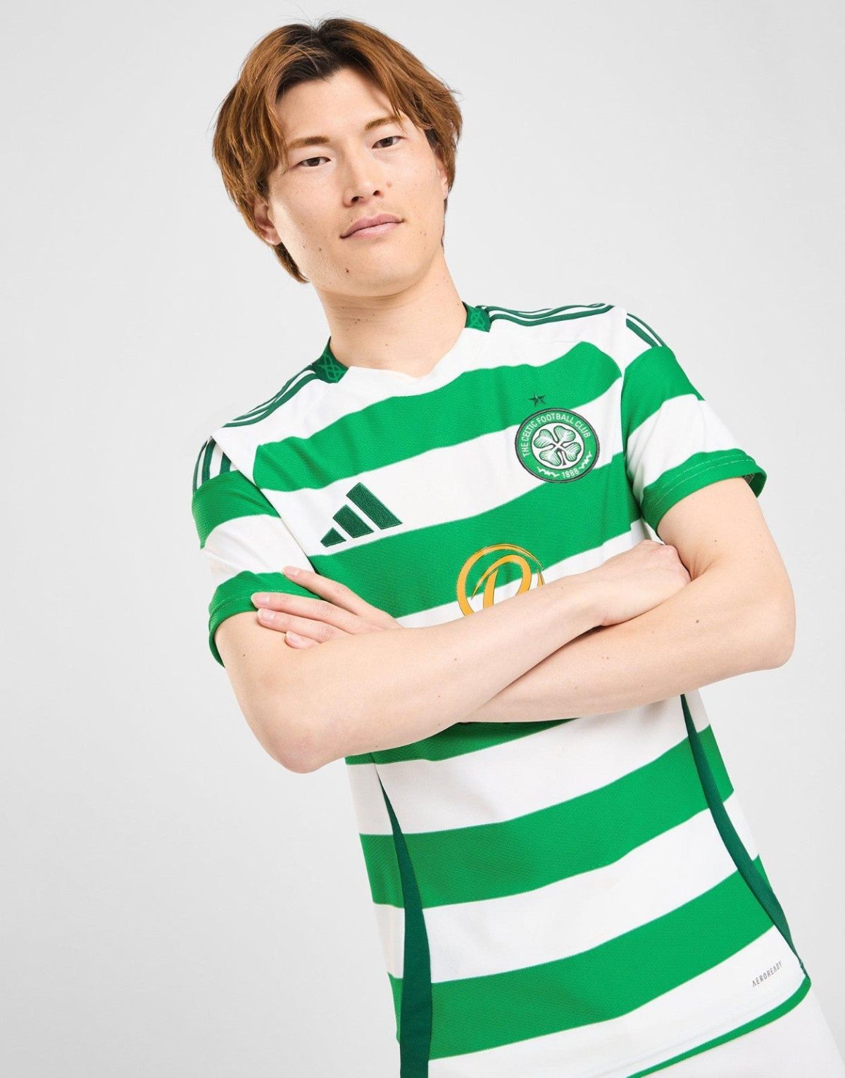 Person wearing a green and white Celtic FC jersey with arms crossed on a light background.